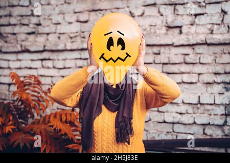 Ragazza nel cortile che tiene gonfiabile palloncino con una faccia malvagia nelle sue mani fuori happy halloween concetto Holiday card Street style Costume stagione d'autunno Foto Stock