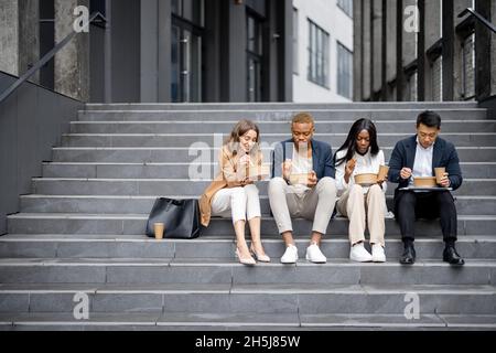 Il team di lavoro parla, mangia e beve sulle scale Foto Stock