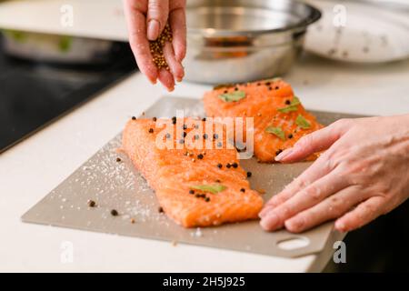 La mano femminile cosparge un pezzo di filetto di salmone adagiato su un tagliere con spezie Foto Stock