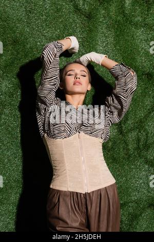 modello giovane in blusa con stampa zebra, corset e guanti appoggiati su sfondo erboso Foto Stock