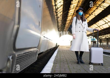 Donna turistica mascherata alla stazione ferroviaria. Turismo durante un concetto pandemico. Misure di prevenzione dei virus nei trasporti pubblici Foto Stock