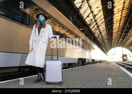 Donna turistica mascherata alla stazione ferroviaria. Turismo durante un concetto pandemico. Misure di prevenzione dei virus nei trasporti pubblici Foto Stock