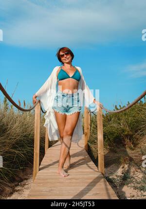 Giovane donna in copertina bianca e jeans pantaloncini una passerella sopra le dune Foto Stock