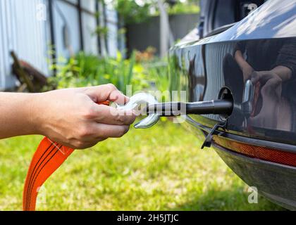 La mano di un uomo aggancia una fune di traino ad un gancio di traino in un'autovettura, da vicino Foto Stock