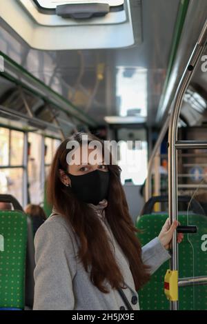 Giovane passeggero europeo donna che indossa una maschera facciale e guarda la macchina fotografica in autobus Foto Stock