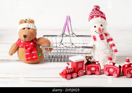 Anno nuovo, concetto di vendite natalizie. Giocattoli di Capodanno vicino al cestino dello shopping su sfondo bianco. Foto Stock