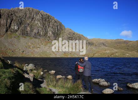 Due persone che godono la vista di Stickle tarn e Pavey Ark nel parco nazionale Lake District, Cumbria, Inghilterra, Regno Unito. Foto Stock