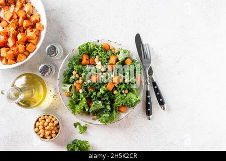 Insalata vegana sana con patate dolci arrostite e kale su sfondo grigio di cemento, vista da tavolo con spazio copia Foto Stock