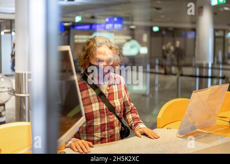 Il turista indossa una maschera FFP2 presso un banco di reclamo schermato in un aeroporto. Foto Stock