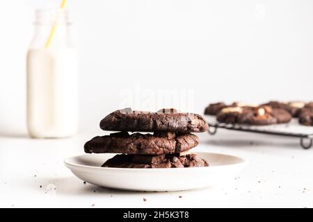 accatastate biscotti al cioccolato fondente con una bottiglia di latte sullo sfondo e un vassoio di biscotti Foto Stock