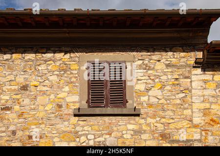 Persiane marroni sulla finestra contro un rustico muro di pietra. Vecchio esterno di una casa di villaggio mediterraneo con finestra vintage chiusa in legno wit Foto Stock