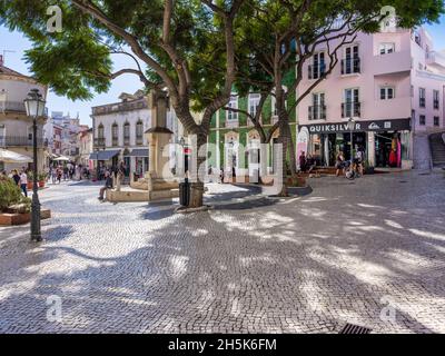 Lagos, Algarve, Portogallo - Novembre 10 2021: Piazza Luis de Camoes con turisti che godono l'autunno ombreggiato da alberi maturi dal primo mem di guerra mondiale Foto Stock