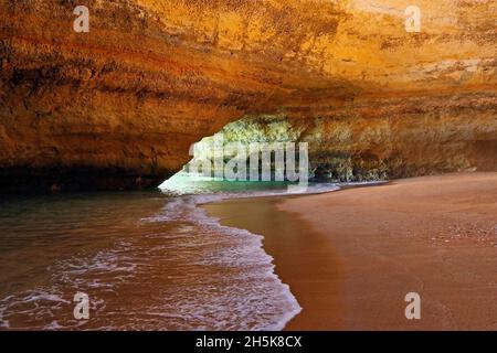 Formazioni rocciose di arenaria, arco di mare lungo la costa oceanica dell'Algarve con surf e spiaggia di sabbia a bassa marea Foto Stock