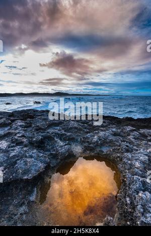 Formazioni rocciose vulcaniche e luce dorata riflesse in una piscina marea sulla spiaggia a Pointe des Chateaux sotto un cielo nuvoloso Foto Stock