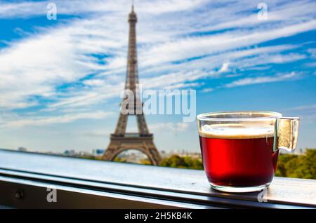 Tazza di vetro di caffè o tè sul balcone con vista sulla Torre Eiffel e sullo sfondo dello skyline di Parigi. Vista soleggiata di un bicchiere di tè con vista sulla Torre Eiffel Foto Stock