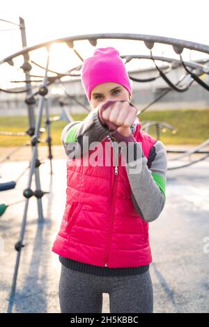 Giovane donna vestita in fitness vestiario boxing con le mani in pugni e fa pugni Foto Stock