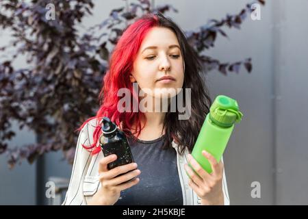 La donna sceglie tra due tipi di bottiglie d'acqua riutilizzabili. Bottiglia d'acqua in alluminio e silicone per l'abitudine di bere tutti i giorni. Stile di vita sostenibile Foto Stock
