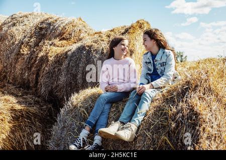 Due giovani sorelle trascorrono del tempo di qualità insieme mentre si siedono su balle di fieno nella loro fattoria familiare; Alcomdale, Alberta, Canada Foto Stock