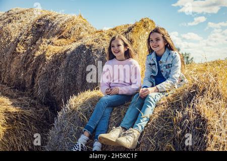 Due giovani sorelle trascorrono del tempo di qualità insieme mentre si siedono su balle di fieno nella loro fattoria familiare; Alcomdale, Alberta, Canada Foto Stock