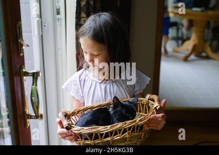 La bambina si alza su una grande porta di vetro con un piccolo gattino nel cestino Foto Stock