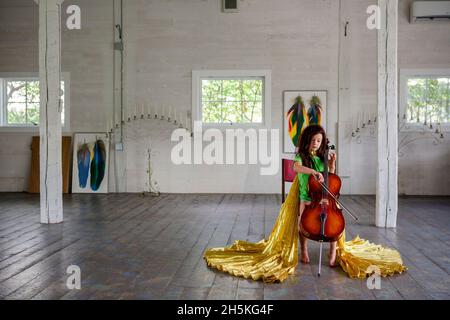 Un bambino piccolo in oro mantello suona violoncello in una grande stanza vuota Foto Stock
