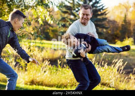 Padre che gioca con i suoi due figli in un parco in autunno; St. Albert, Alberta, Canada Foto Stock