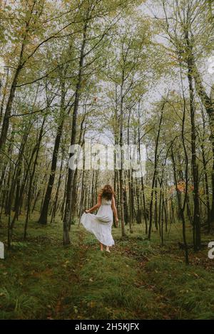 Donna in abito bianco che scorre attraverso una radura nel bosco. Foto Stock