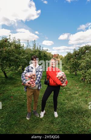 Anni dell'adolescenza felici che tengono i sacchetti delle mele raccolte fresche in un frutteto. Foto Stock