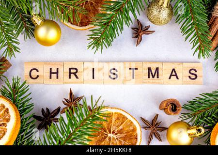 Testo di Natale in legno con rami di abete verde, baubles dorati, arance e spezie come decorazione stagionale natale su sfondo bianco per il saluto ca Foto Stock