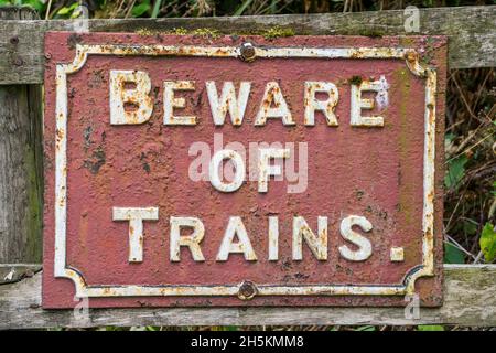 Primo piano del vecchio cartello ferroviario d'epoca isolato all'aperto, avvertendo il pubblico di fare attenzione ai treni, Regno Unito. Foto Stock