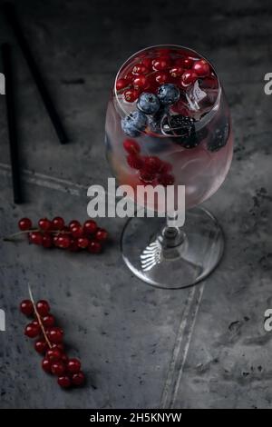 Fresco cocktail estivo con frutti di bosco in bicchiere di vino con ribes rosso e mirtilli su sfondo grigio argilloso Foto Stock