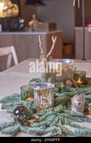 Centro di Natale in stile rustico preparato per una cena di Natale in famiglia con una figura di renna e candele accese su un tavolo di legno. Concetto di natale Foto Stock