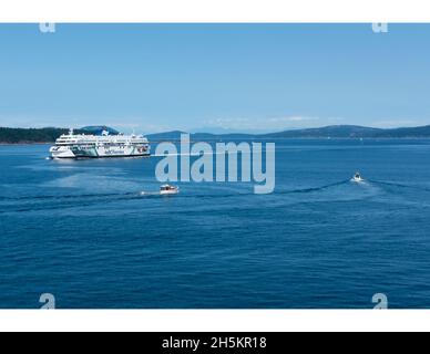 Due piccole imbarcazioni lasciano un ampio ormeggio per il traghetto Coastal Celebration sulla strada per Swartz Bay (Victoria). Foto Stock