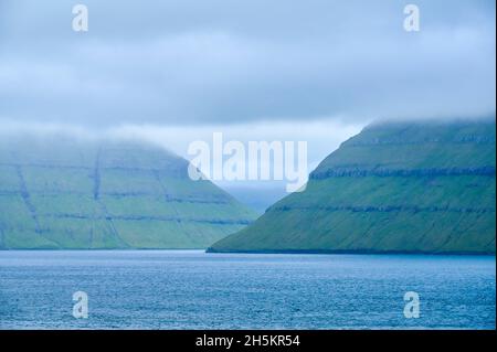 Vista dal traghetto Norrona isola quando si guida attraverso le Isole Faroe, con nuvole tempesta sul paesaggio montano; Isole Faroe, Danimarca Foto Stock