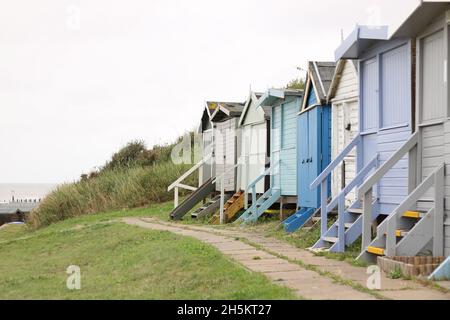 30 agosto 2021 - Essex UK: Fila di vecchie capanne da spiaggia con erba in primo piano Foto Stock