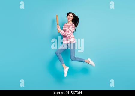 La dimensione del corpo a tutta lunghezza vista di ragazza allegra che salta avendo pipistrello di combattimento divertente isolato su sfondo di colore blu chiaro Foto Stock