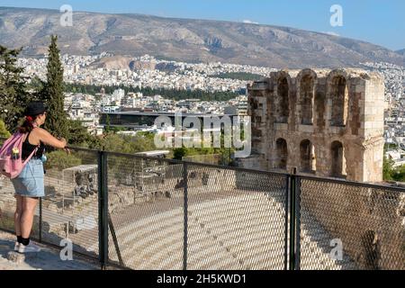 La giovane donna ammirerà la vista sull'Odeon di Erode Attico (o Erodion), l'antico teatro greco, il Museo dell'Acropoli e la città di Atene Foto Stock