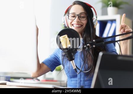 Donna presentatrice sorridente in cuffie che parla nel microfono in studio Foto Stock