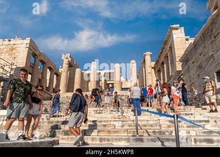 Turisti di fronte alla Propylea, la porta monumentale per l'Acropoli di Atene, Grecia. Vista panoramica sulla facciata, giorno di sole, cielo blu, nuvole Foto Stock