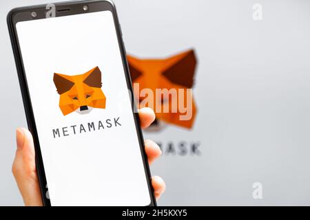 Ucraina, Odessa - Ottobre, 9 2021: Tenere la mano mobile con l'app MetaMask in esecuzione sullo schermo dello smartphone con il logo MetaMask sullo sfondo. MetaMask è così Foto Stock