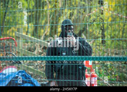 Wendover, Regno Unito. 9 novembre 2021. Il responsabile del National Eviction Team (NET) Enforcement Agent che sta guidando una squadra di baliffi che tenta di sgombrare l'attivista ambientale Swampy e altri tunnellers da sotto il campo DI GUERRA della resistenza attiva di Stop HS2 Wendover. La rete regolarmente film membri della stampa, pubblico e manifestanti a piedi sui sentieri pubblici vicino a siti HS2. La rete ha suturato un certo numero di manifestanti di Stop HS2 e di stampa, ma indossano occhiali scuri anche di notte e coprono il loro volto nel tentativo di non essere riconosciuti. Credit: Maureen McLean/Alamy Foto Stock