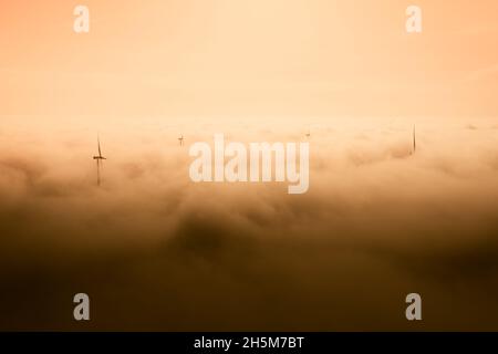 Parchi eolici che sporgono sopra le nuvole, vista aerea di eliche a turbina lontane Foto Stock