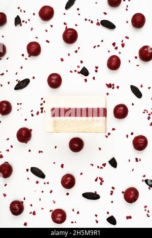 Vista dall'alto della deliziosa fetta di torta di mousse di ciliegia con gli strati visualizzati e gli ingredienti della ricetta disposti su sfondo bianco. Menu del ristorante e concetto di pasticceria in stile piatto. Foto Stock