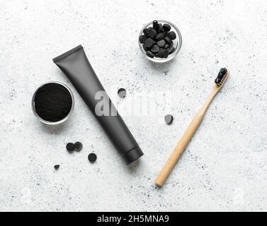 Spazzolino da denti in bambù, tubo per dentifricio, ciotole con polvere di dente di carbone attivo e pillole su sfondo chiaro Foto Stock