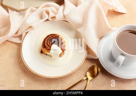 Piatto con gustoso rotolo di cannella e tazza di caffè su sfondo beige Foto Stock