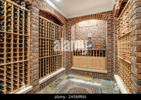 Una grande cantina di vini in una casa di lusso con pareti in mattoni e rack in legno. Foto Stock