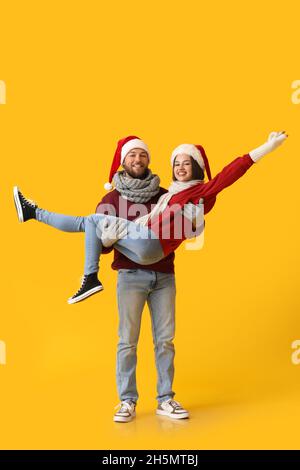 Felice giovane coppia in eleganti abiti invernali e cappelli Babbo Natale su sfondo colorato Foto Stock