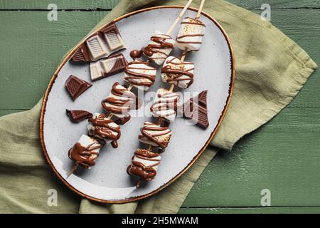 Piatto di gustosi marshmallows grigliati su sfondo di legno verde Foto Stock