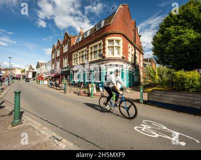 Ciclisti e pedoni passano negozi indipendenti, caffetterie e ristoranti in East Street a Bedminster, Bristol. Foto Stock