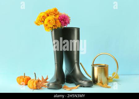 Composizione con stivali di gomma, fiori, annaffiatoio e zucche su sfondo colorato Foto Stock